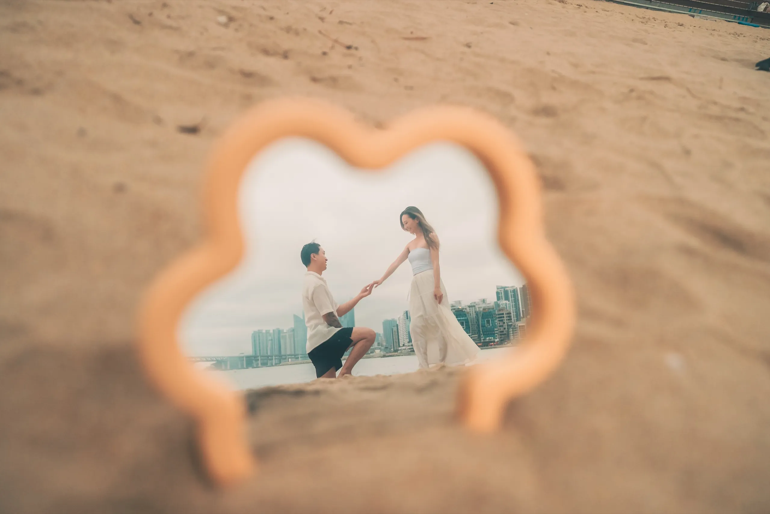 A proposal on the sand, caught in a small cloud-shaped mirror